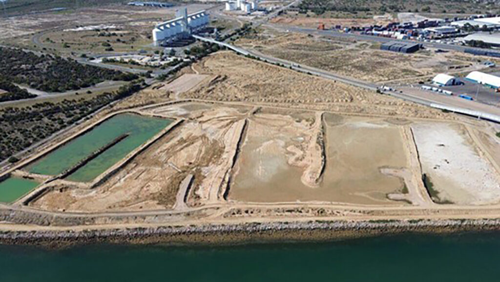 Aerial view of an industrial site featuring two rectangular ponds, arid land, nearby roads, and industrial buildings in the background.